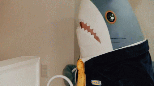 a woman in a yellow shirt holds a stuffed shark on top of a bed