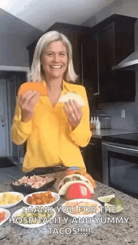 A Woman In A Yellow Shirt Is Holding A Taco In Her Hands And Smiling . GIF