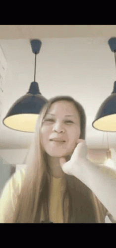 A Woman In A Yellow Shirt Is Making A Funny Face With Her Hand GIF