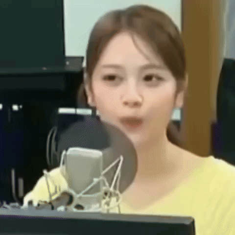 A Woman In A Yellow Shirt Is Sitting In Front Of A Microphone . GIF