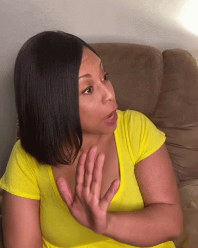 A Woman In A Yellow Shirt Is Sitting On A Couch Making A Face GIF