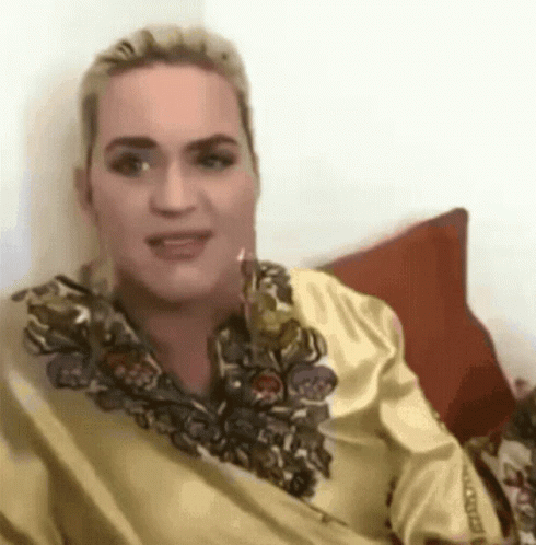 A Woman In A Yellow Shirt Is Sitting On A Couch With A Red Pillow . GIF