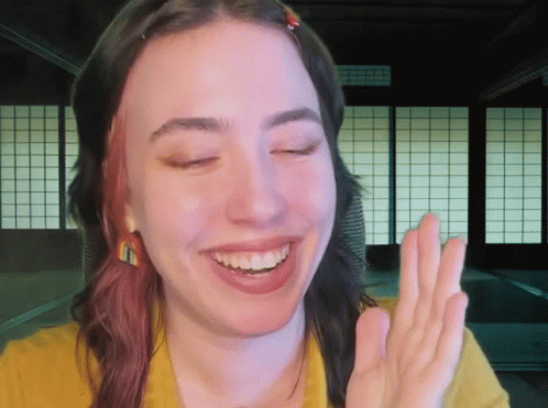 A Woman In A Yellow Shirt Is Smiling And Making A Peace Sign GIF