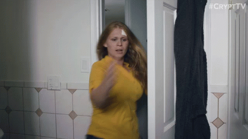 A Woman In A Yellow Shirt Is Standing In A Doorway With #Crypttv Written On The Bottom Right GIF