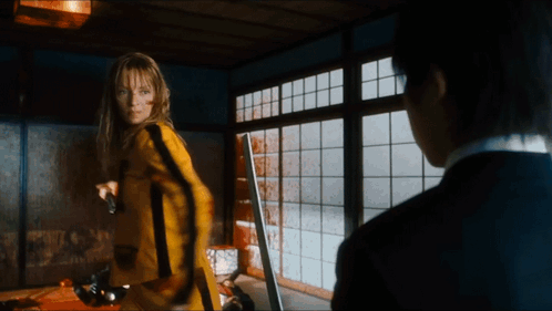 A Woman In A Yellow Suit Is Holding A Gun GIF