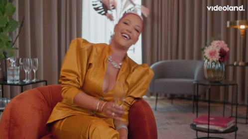 A Woman In A Yellow Suit Is Sitting In A Chair With A Videoland Logo In The Corner GIF