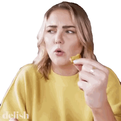 a woman in a yellow sweater is eating a piece of food and the word delish is on the bottom right