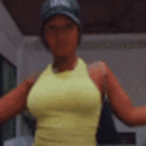 A Woman In A Yellow Tank Top And A Black Hat Is Standing With Her Arms Outstretched . GIF