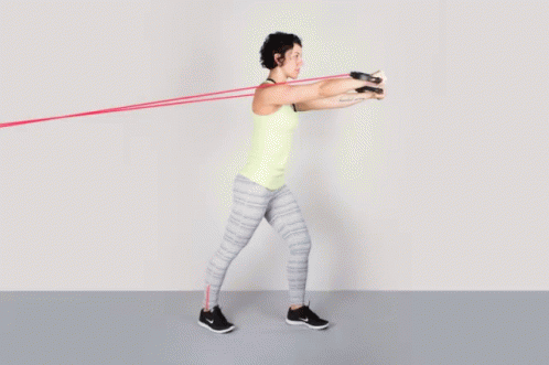 A Woman In A Yellow Tank Top Is Doing Exercises With A Resistance Band GIF