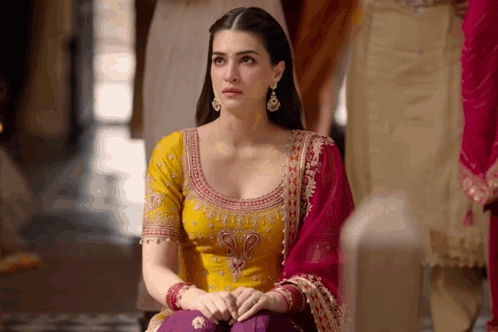 A Woman In A Yellow Top And Purple Pants Sits On A Bench GIF