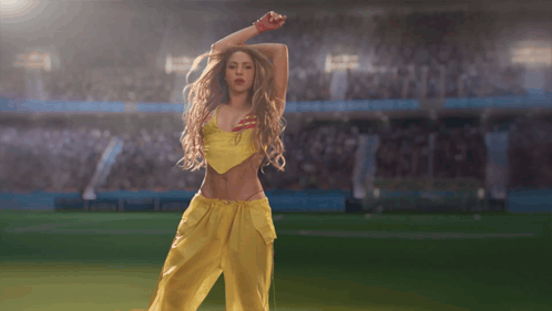 a woman in a yellow top and yellow pants is dancing on a soccer field