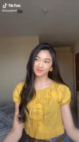 A Woman In A Yellow Top Is Dancing In A Room With A Tiktok Watermark GIF
