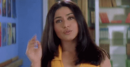 A Woman In A Yellow Top Is Standing In Front Of A Bookshelf And Smoking A Cigarette . GIF