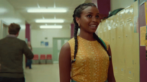 A Woman In A Yellow Top Stands In A Hallway Next To Lockers GIF