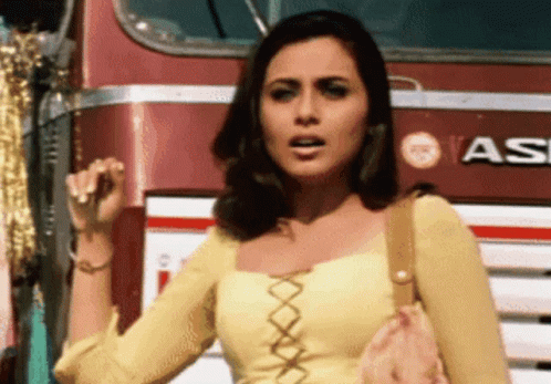 A Woman In A Yellow Top Stands In Front Of A Red Bus That Says Vasi GIF
