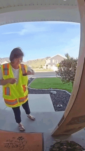 A Woman In A Yellow Vest Is Standing In Front Of A Door With A Welcome Mat GIF