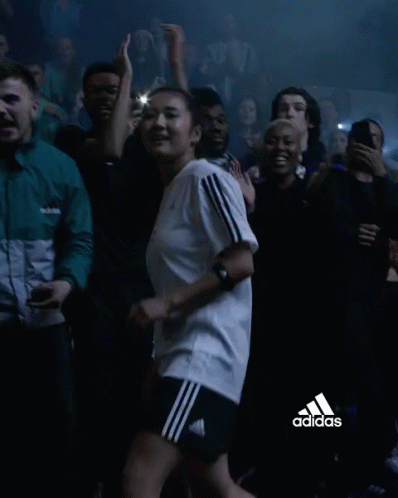 a woman in an adidas shirt is dancing in a crowd of people