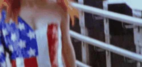 A Woman In An American Flag Dress Is Standing Next To A Railing . GIF