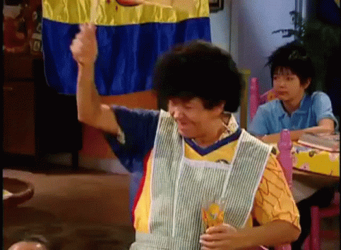 A Woman In An Apron Is Sitting At A Table With A Glass Of Orange Juice . GIF