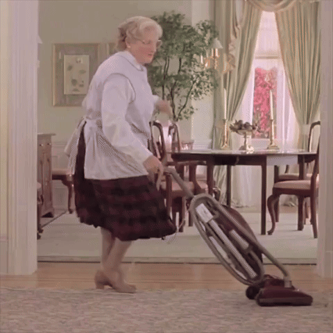 A Woman In An Apron Is Using A Vacuum Cleaner In A Dining Room GIF