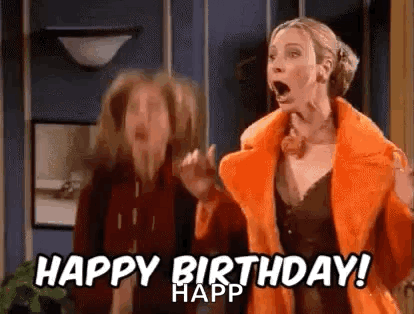 A Woman In An Orange Coat Is Standing Next To Another Woman In A Living Room . GIF