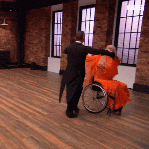 A Woman In An Orange Dress Is Dancing With A Man In A Black Suit GIF