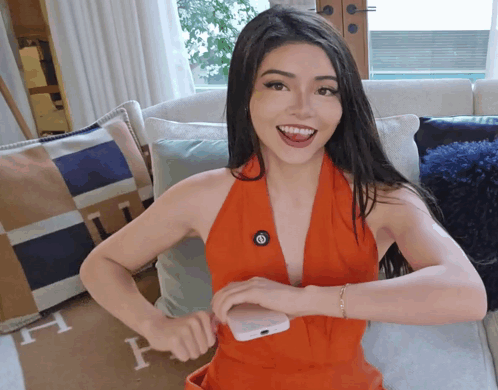 A Woman In An Orange Dress Is Sitting On A Couch With A Hermes Rug GIF