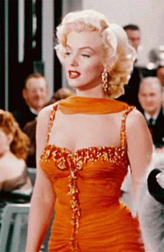 A Woman In An Orange Dress Is Standing In A Crowd GIF