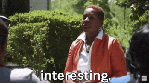A Woman In An Orange Jacket Is Talking To A Man In A Park And The Woman Is Saying Interesting . GIF