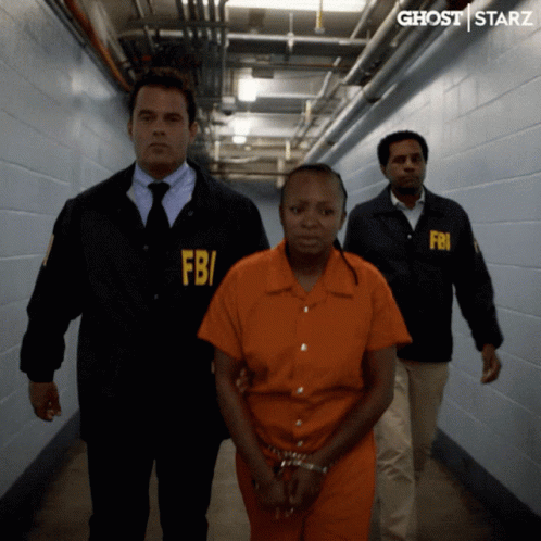 A Woman In An Orange Jumpsuit Is Being Escorted By Two Men In Fbi Uniforms GIF
