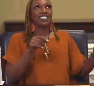 A Woman In An Orange Shirt Is Sitting At A Table Holding A Pair Of Earrings . GIF