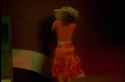 A Woman In An Orange Skirt Is Dancing In A Dark Room . GIF