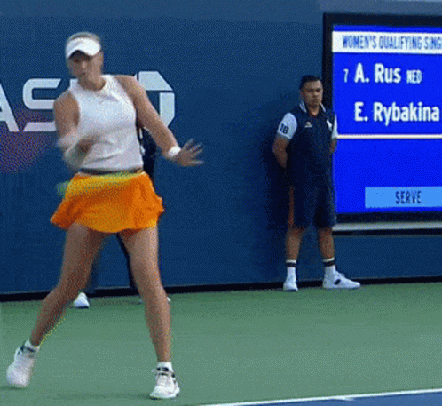 A Woman In An Orange Skirt Is Playing Tennis On A Tennis Court GIF