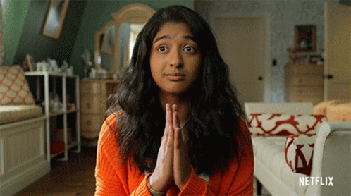 A Woman In An Orange Sweater Is Praying With Netflix Written On The Bottom Right GIF