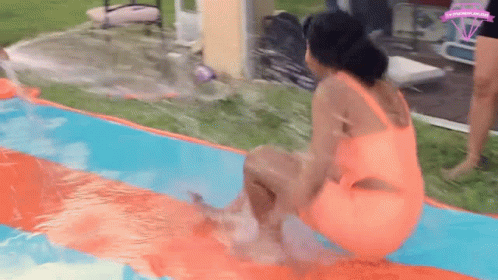 A Woman In An Orange Swimsuit Is Sitting On Top Of A Water Slide In A Pool . GIF