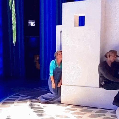 A Woman In Blue Overalls Is Peeking Out From Behind A Wall GIF