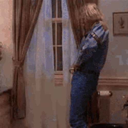 A Woman In Blue Overalls Is Standing In Front Of A Window . GIF
