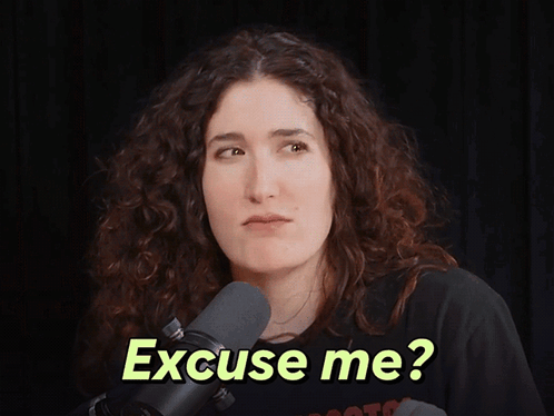 A Woman In Front Of A Microphone With The Words " Excuse Me " On Her Face GIF