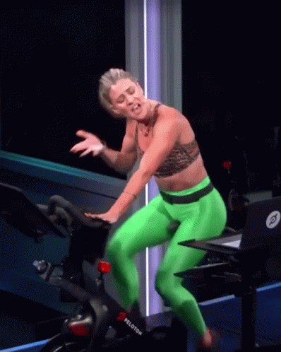 A Woman In Green Pants Is Riding A Peloton Exercise Bike GIF