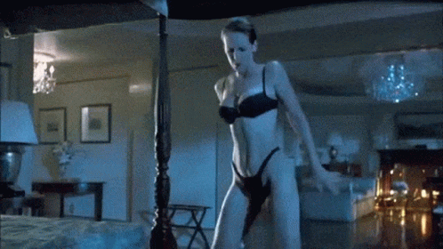 A Woman In Lingerie Is Standing Next To A Bed In A Bedroom . GIF