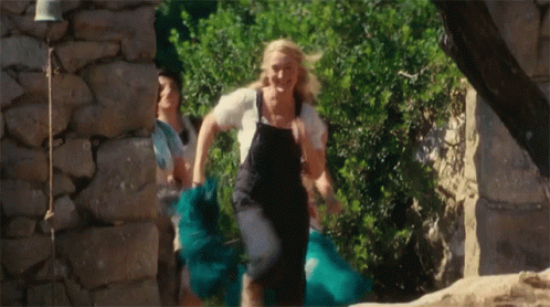 A Woman In Overalls Is Running With A Blue Skirt GIF