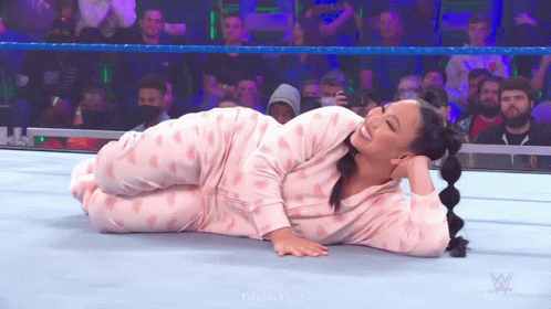 A Woman In Pink Pajamas Is Laying On The Ground In A Wrestling Ring . GIF