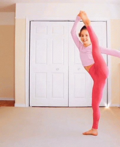 a woman in pink pants is doing a split in front of a white door