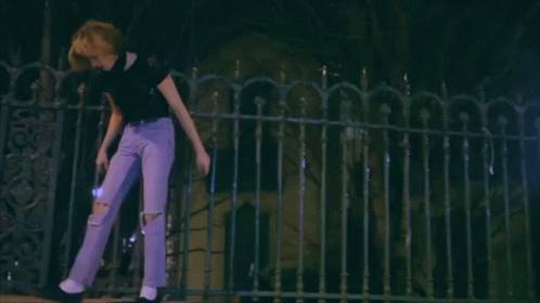 a woman in purple jeans is walking across a fence at night