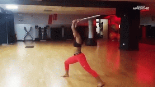 A Woman In Red Pants Is Holding A Sword In A Gym With The Words Awesome On The Bottom GIF