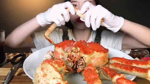 A Woman In White Gloves Is Eating A Large Red Crab GIF