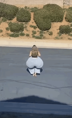 A Woman In White Pants Is Squatting Down On The Side Of The Road GIF