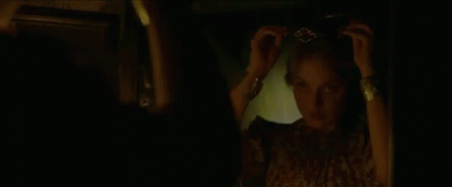 A Woman Is Adjusting Her Hair In Front Of A Mirror In The Dark . GIF