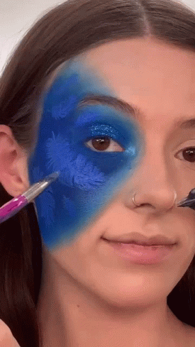 A Woman Is Applying Blue Paint To Her Face With A Brush . GIF
