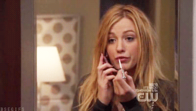 A Woman Is Applying Lip Gloss While Talking On A Cell Phone .. GIF